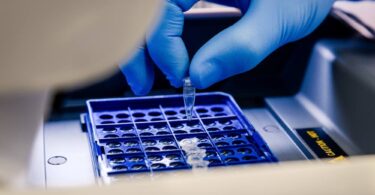 Laboratory technician loading a sample tube into a sequencing instrument for molecular analysis.