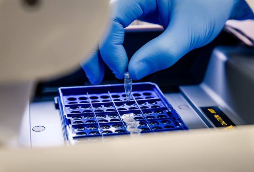 Laboratory technician loading a sample tube into a sequencing instrument for molecular analysis.