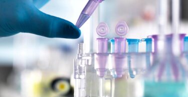 Gloved hand placing a microtube into a rack in a clinical research lab.