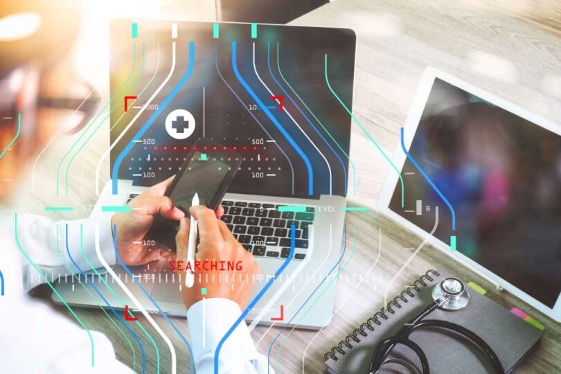Doctor using smartphone and laptop with digital health interface overlay, representing continuous glucose monitoring technology
