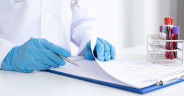 Doctor in medical gloves reviewing clinical trial documents with blood samples nearby.