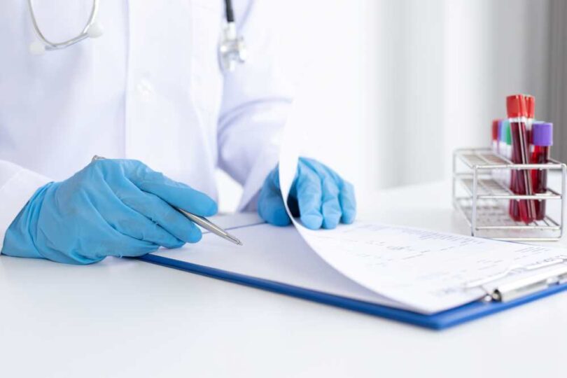 Doctor in medical gloves reviewing clinical trial documents with blood samples nearby.