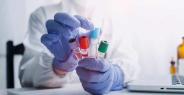 “Scientist wearing protective gloves holding multiple blood sample vials in a haematology laboratory.”
