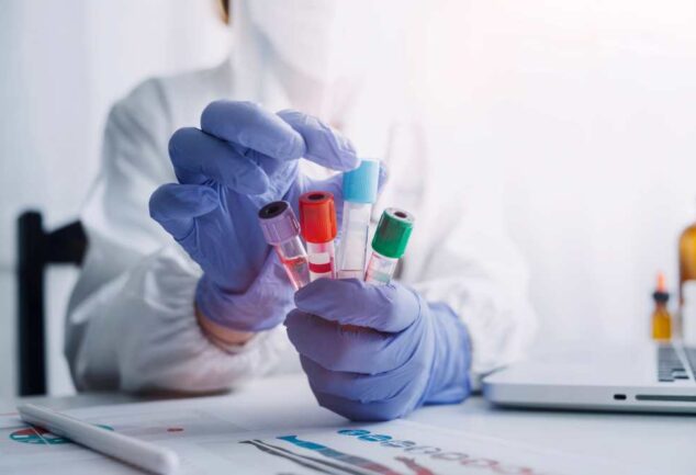 “Scientist wearing protective gloves holding multiple blood sample vials in a haematology laboratory.”