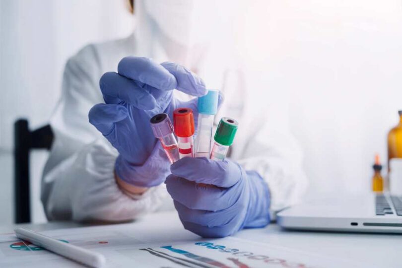“Scientist wearing protective gloves holding multiple blood sample vials in a haematology laboratory.”