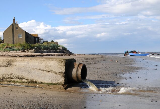 Wastewater flowing from a sewage outfall pipe onto a shoreline