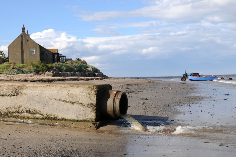 Wastewater flowing from a sewage outfall pipe onto a shoreline