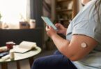 Wearable glucose sensor on an upper arm paired with a smartphone app, illustrating dual glucose-ketone sensor technology