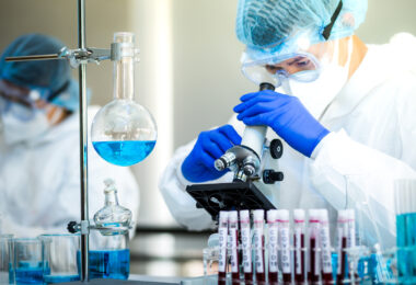 Gloved hand in blue gloves holding a vaccine shot, representing preparation for human clinical trials.