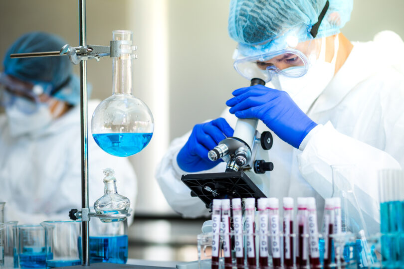 Gloved hand in blue gloves holding a vaccine shot, representing preparation for human clinical trials.