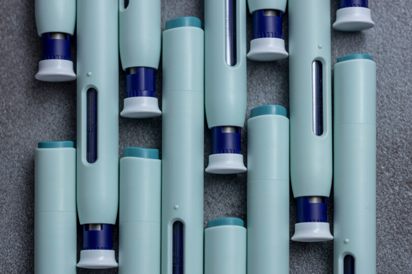 Close-up of several syringe-style self-injection pens arranged on a rustic gray kitchen counter.