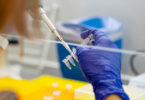 Scientist pipetting a sample into a vial for DNA testing in a laboratory setting.